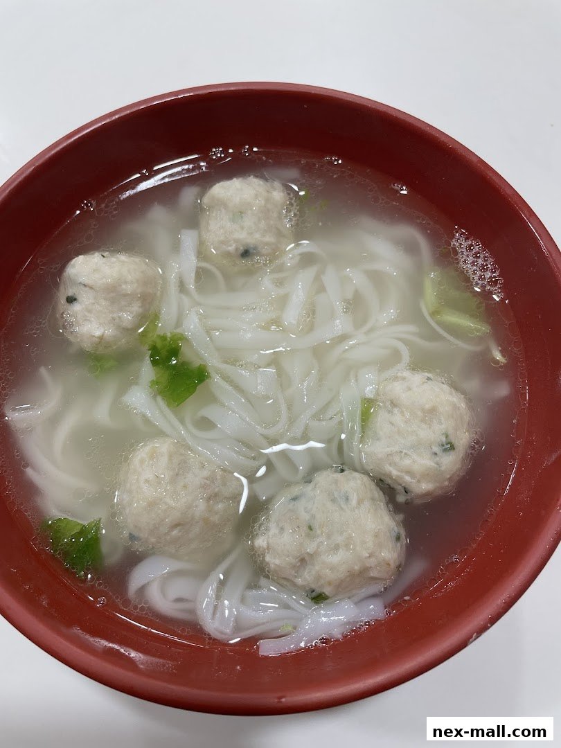A close-up shot of a bowl of noodle soup with fish balls and green herbs.