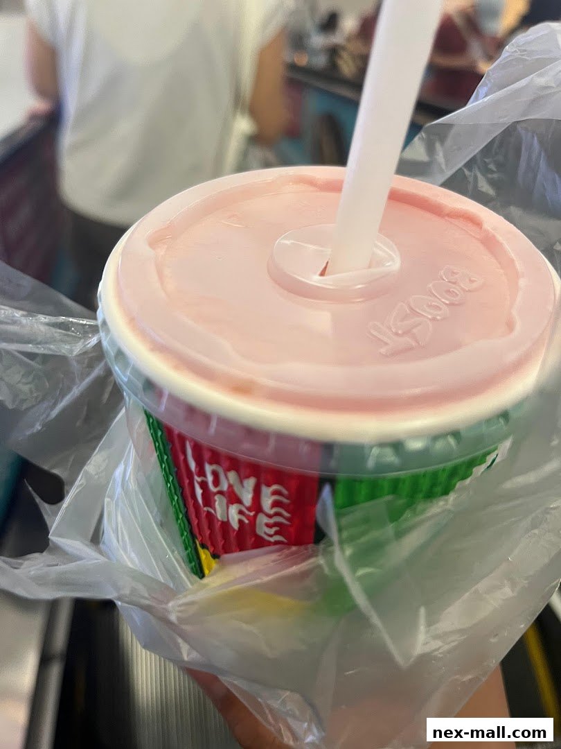 A close-up of a Boost Juice cup with a pink lid and straw, in a plastic bag.