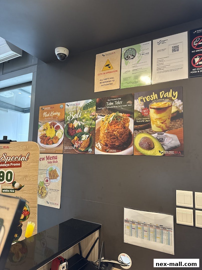 A wall display inside Ayam Penyet Ria featuring food posters, certifications, and a CCTV notice.