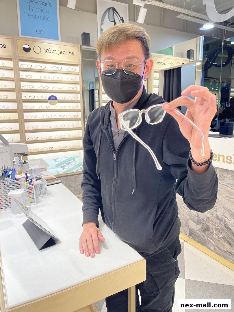 A man in a mask holds up clear-framed glasses in an eyewear store.