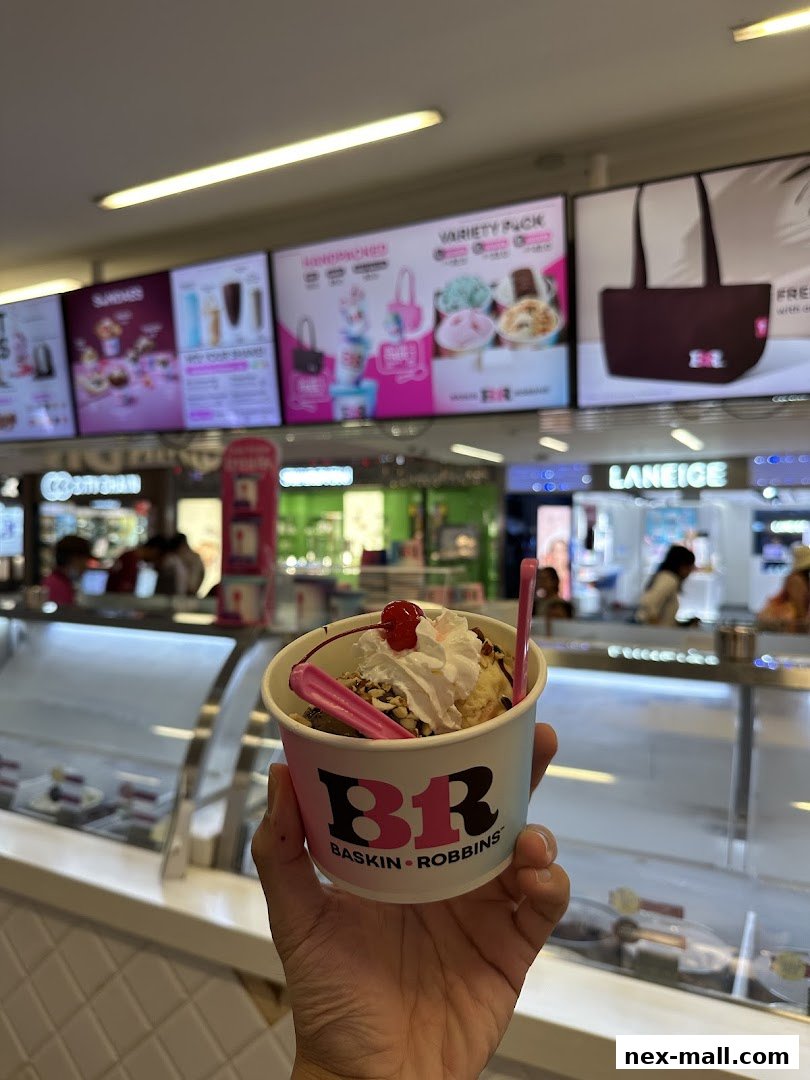 A hand holds a Baskin-Robbins ice cream sundae in front of the shop's displays.