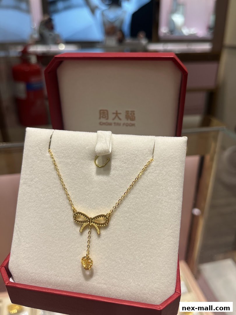 A delicate gold necklace with a bow pendant and a dangling charm, presented in a red jewelry box.