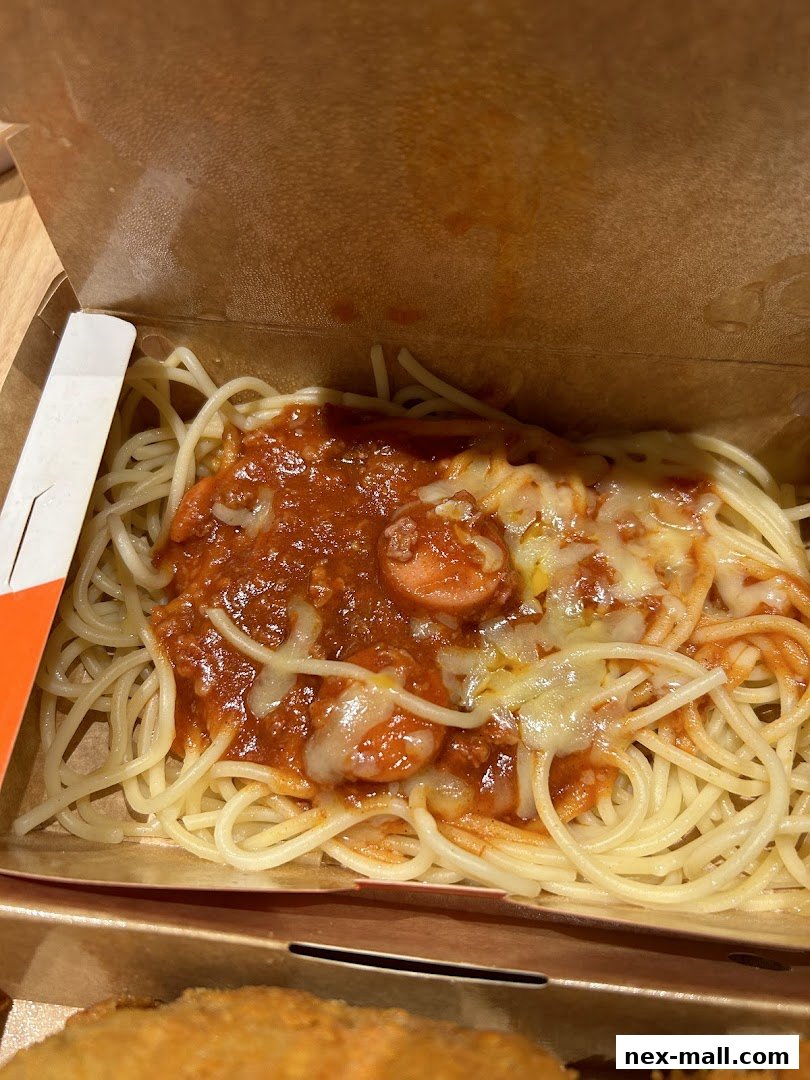 A close-up shot of Jollibee's spaghetti with cheese and hotdog slices in a takeout box.