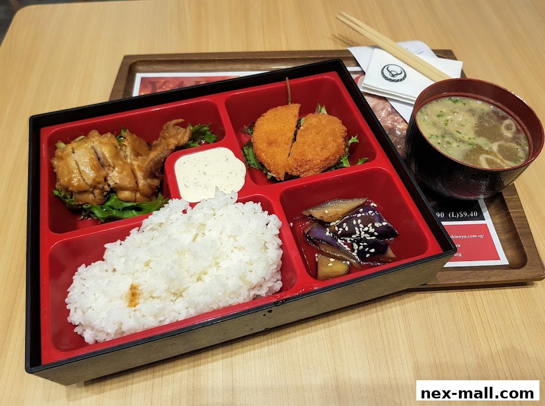 A Yoshinoya bento box with teriyaki chicken, fried item, rice, eggplant, and miso soup.