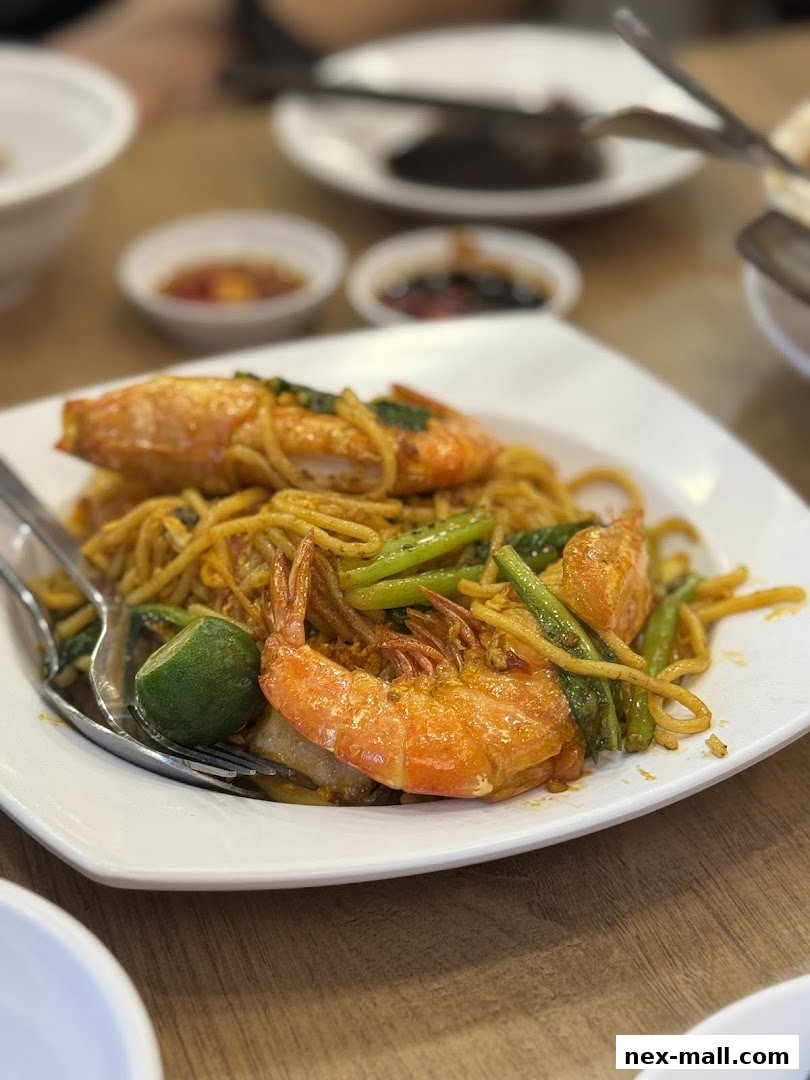 A plate of stir-fried noodles with large prawns and vegetables, served with dipping sauces.