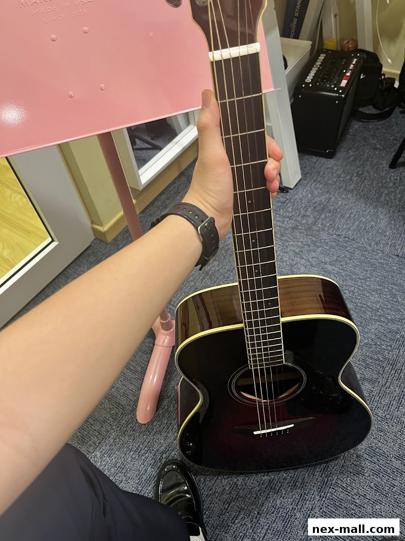 A person holds an acoustic guitar in front of a pink music stand.