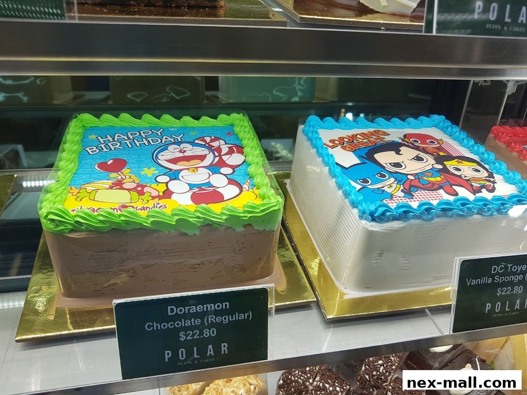 Two decorated cakes, one with Doraemon and the other with DC Comics characters, displayed in a shop.
