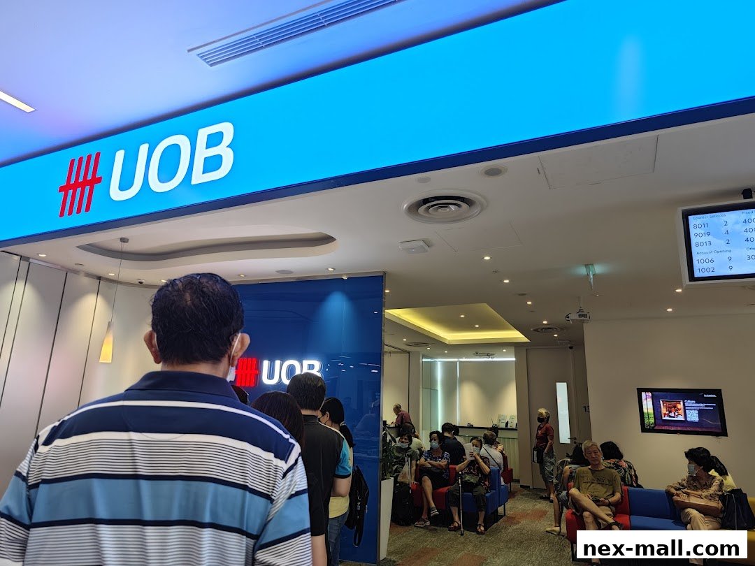 People queue inside a UOB bank branch with a digital display showing queue numbers.