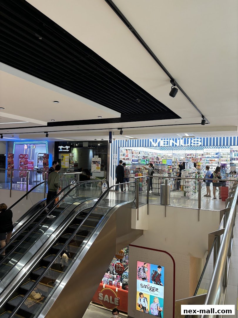 View of a shopping mall interior with escalators and various shops, including Venus Beauty NEX.