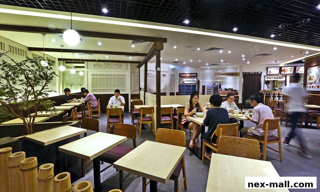 Diners enjoy meals at tables inside a modern, well-lit udon restaurant with Japanese-inspired decor.