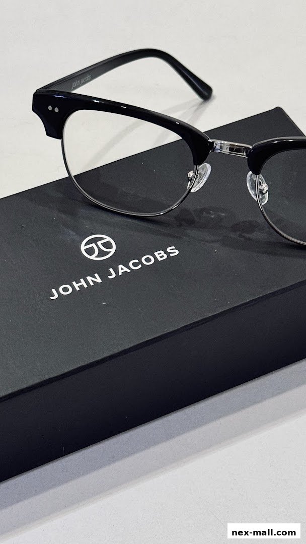 A pair of black John Jacobs eyeglasses rests on a black branded box.
