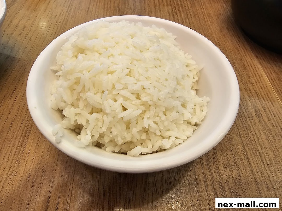 A close-up shot of a white bowl filled with fluffy white rice on a wooden table.
