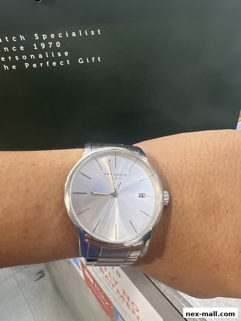 A person wearing a silver Aries Gold watch with a silver dial and date window.