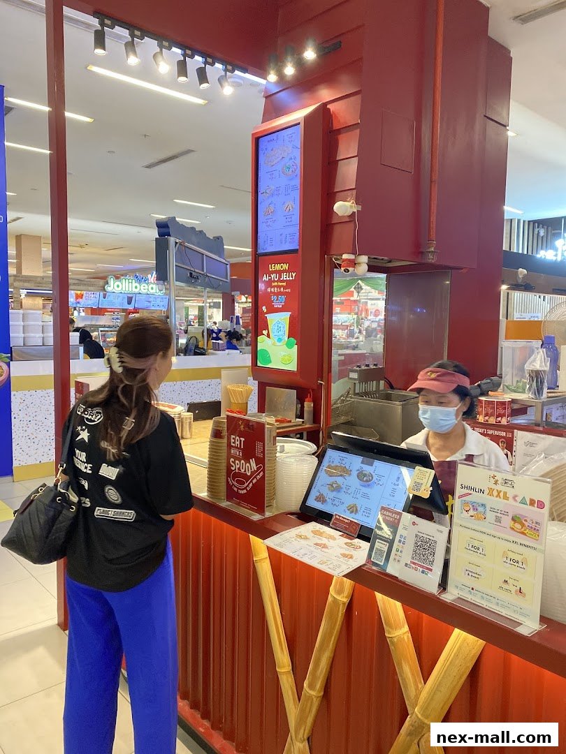 A customer orders at a Shihlin Taiwan Street Snacks counter with a digital menu and promotional materials.