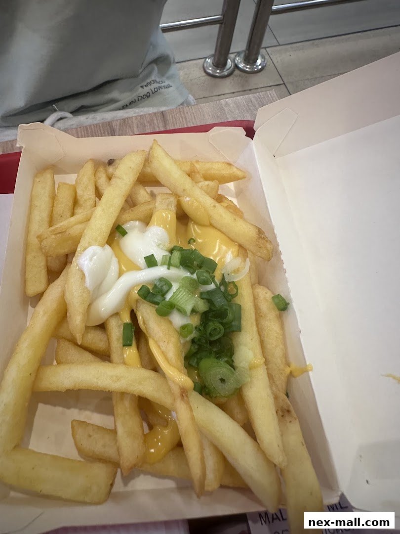 A box of crispy french fries topped with cheese sauce, mayonnaise, and chopped green onions.