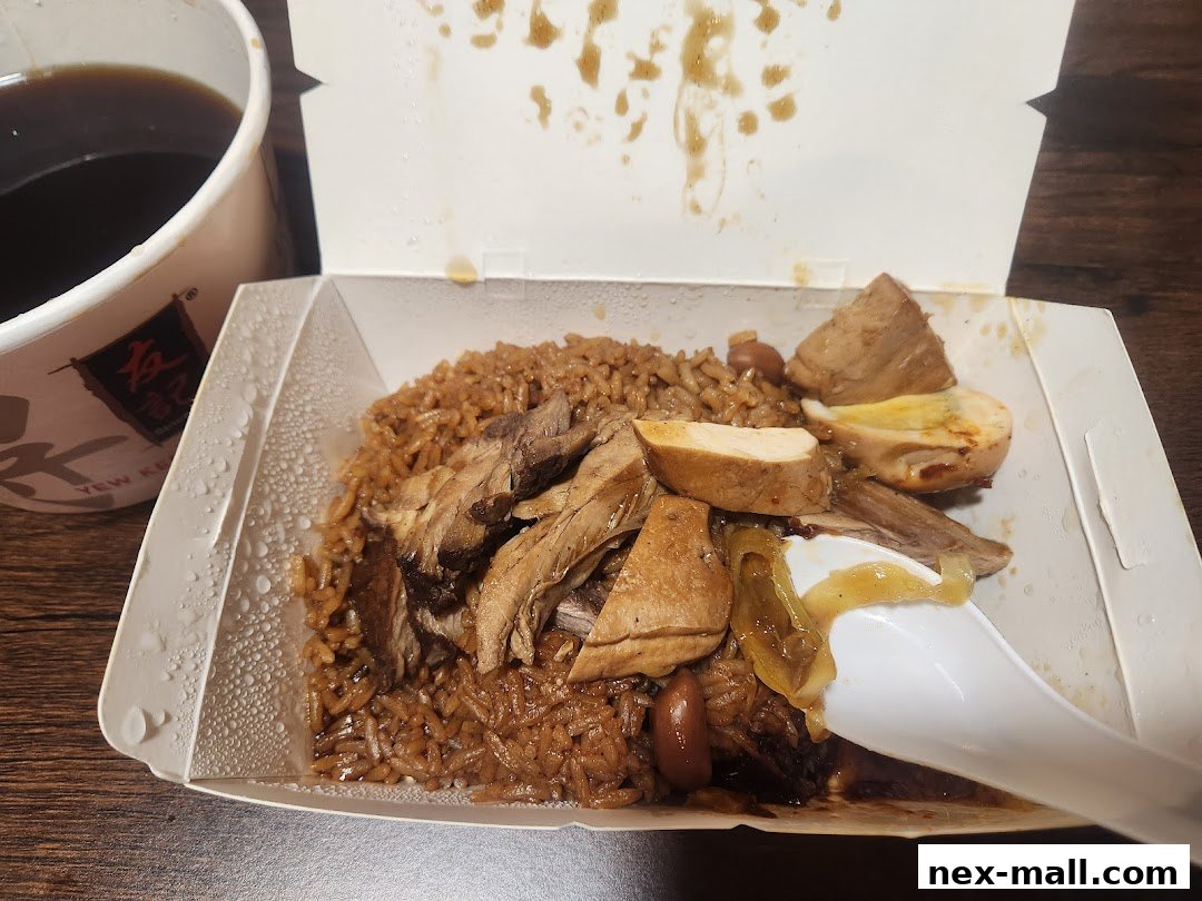 A takeaway box of braised rice with meat and egg, next to a cup of dark beverage.
