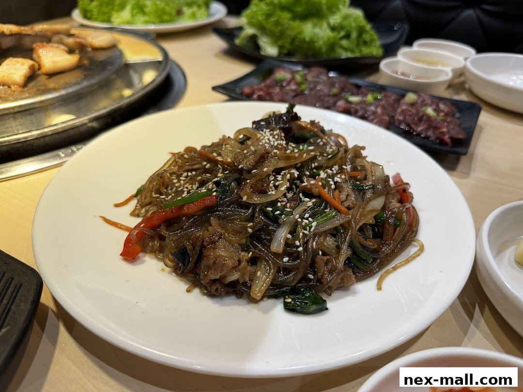 A plate of Korean Japchae noodles with beef, vegetables, and sesame seeds.