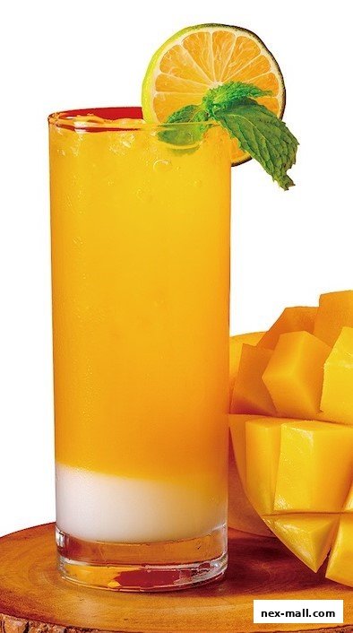 A tall glass of refreshing mango juice with a slice of lime and mint garnish, next to fresh mango chunks.