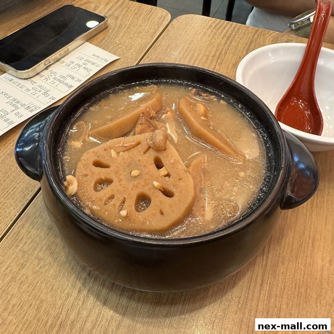 A steaming bowl of lotus root soup with meat and peanuts, served with a receipt and spoon.