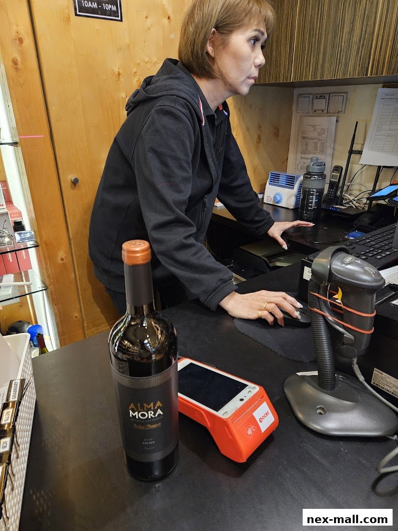 A woman works at a counter with a bottle of wine, payment terminal, and scanner.
