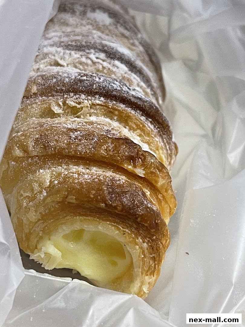 A close-up of a flaky, cream-filled pastry dusted with powdered sugar.