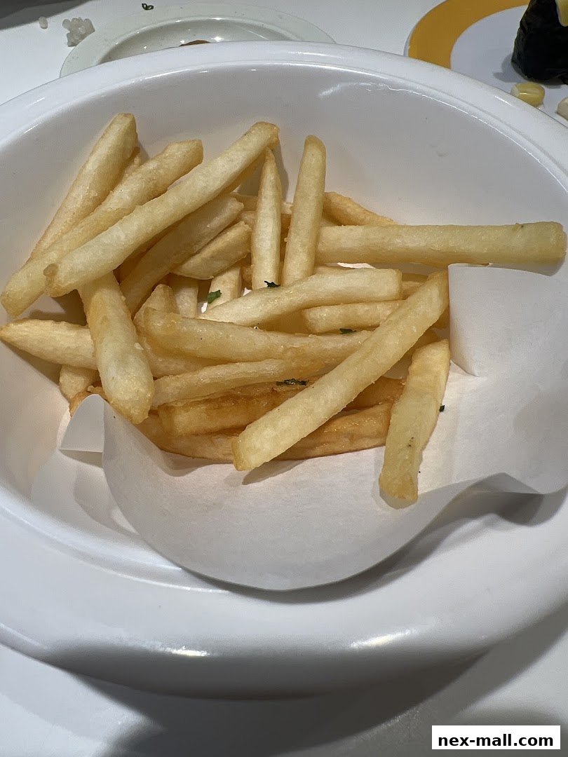 A close-up shot of a bowl filled with golden French fries, garnished with herbs.