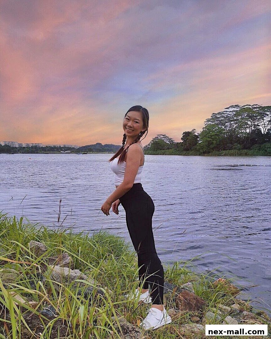 A smiling woman in athletic wear poses by a lake at sunset.