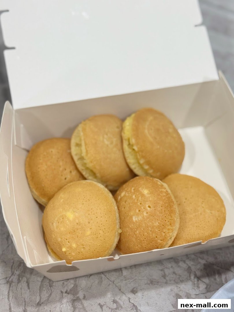 A white box filled with six golden-brown, fluffy pancakes.
