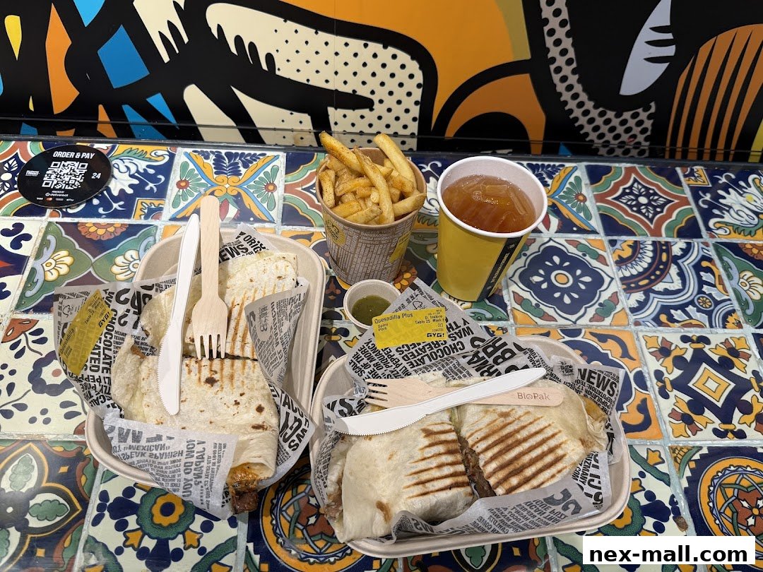 Two burritos, fries, and a drink are displayed on a colorful tiled surface.