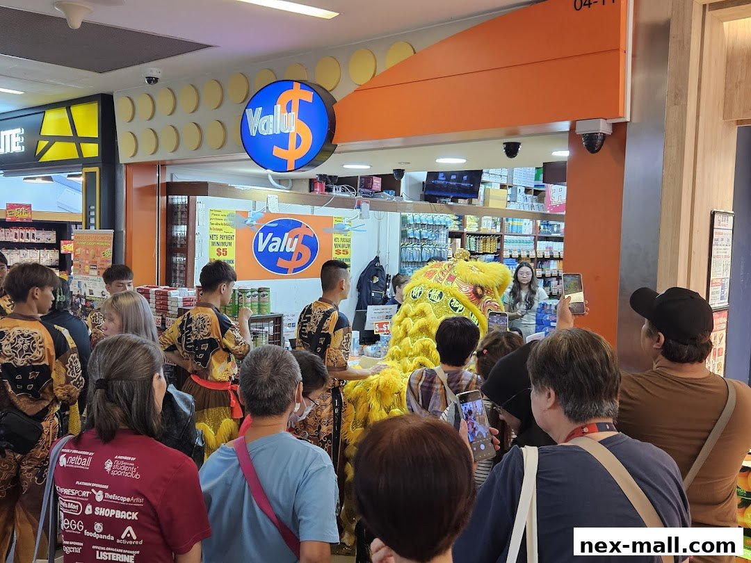 A crowd watches a lion dance performance in front of a Valu store.