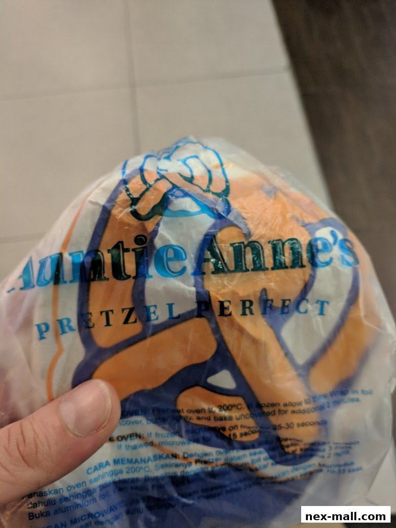 A hand holds a plastic bag with the Auntie Anne's logo and pretzel design.
