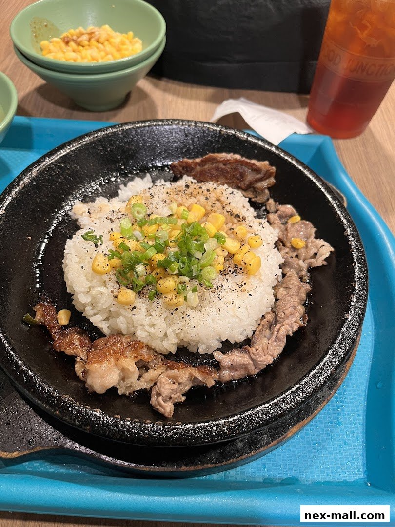 A sizzling hot plate of rice with beef, corn, and green onions, served with a side of corn and iced tea.