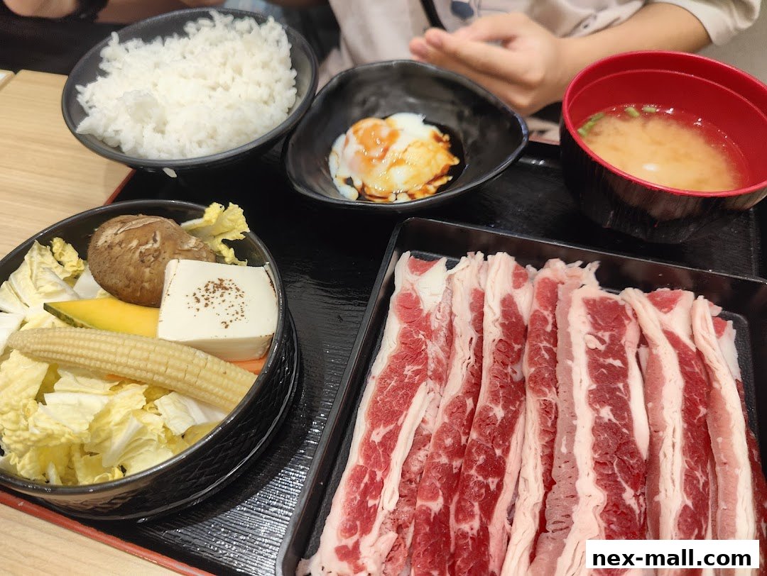A delicious Japanese meal featuring thinly sliced beef, rice, vegetables, miso soup, and a soft-boiled egg.