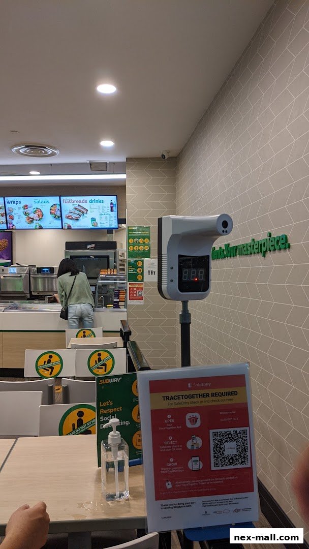 Interior of a Subway restaurant with a temperature scanner and social distancing signs.