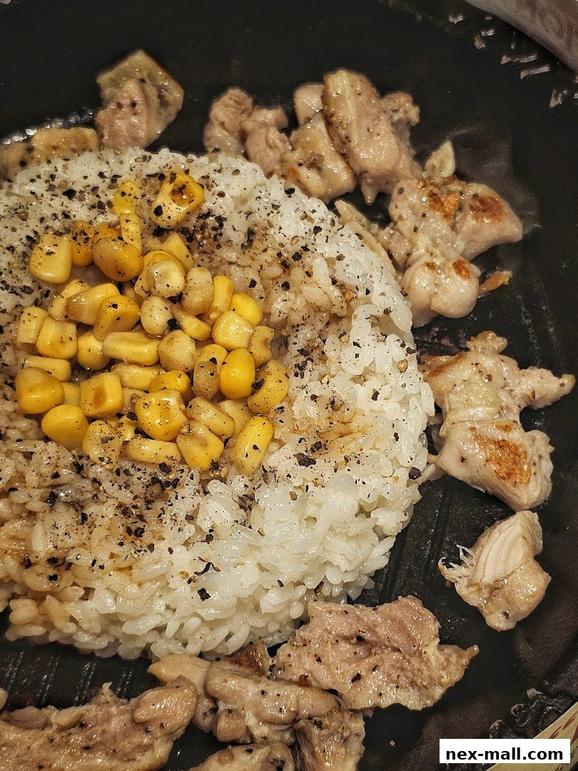 A close-up of a sizzling hot plate with rice, corn, and grilled chicken.