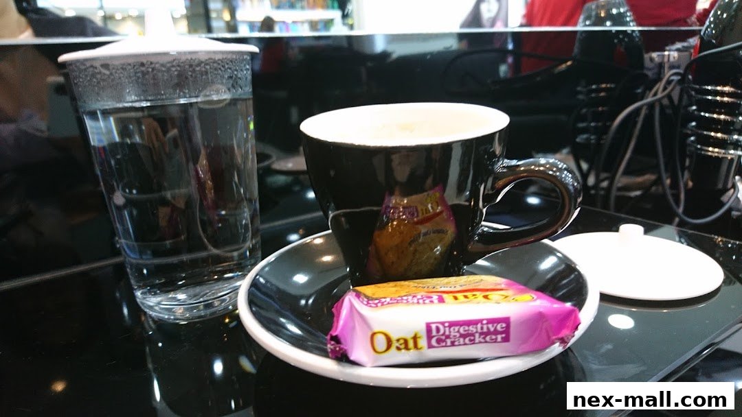 A black coffee cup with a biscuit and a glass of water on a black surface.