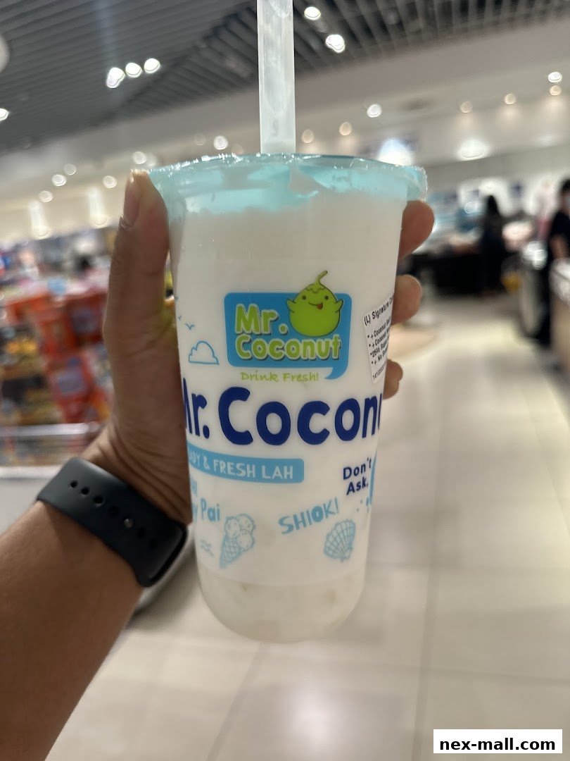 A hand holds a refreshing Mr. Coconut drink with the shop's logo visible.