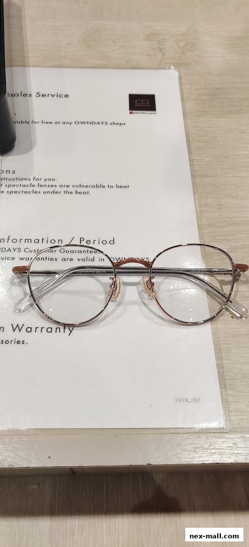A pair of round, rose gold-rimmed glasses rests on a document from OWNDAYS.