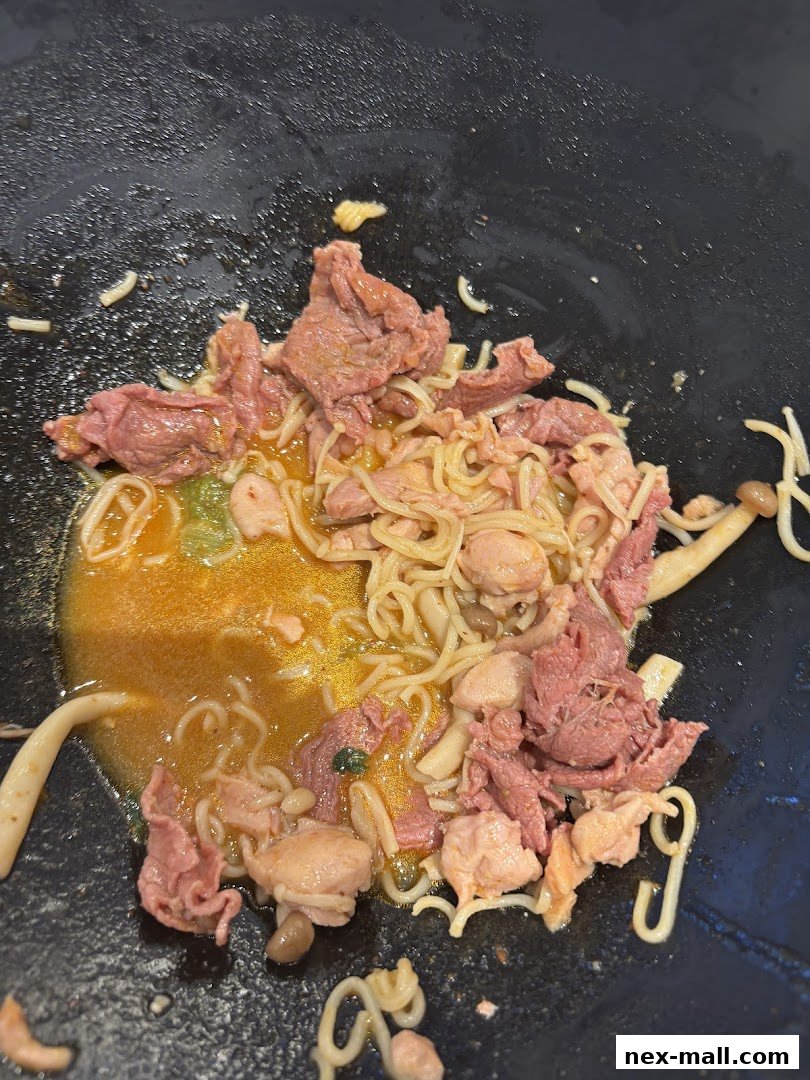 A close-up of a hot pot dish with noodles, beef, chicken, and mushrooms in broth.