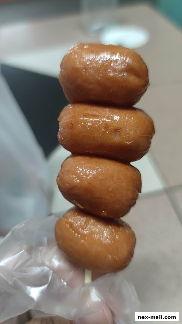 A close-up shot of a skewer with four glistening sausages, held by a gloved hand.