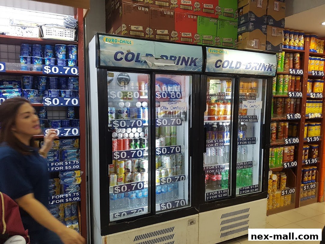 A woman stands in front of refrigerated drink displays and shelves stocked with snacks.