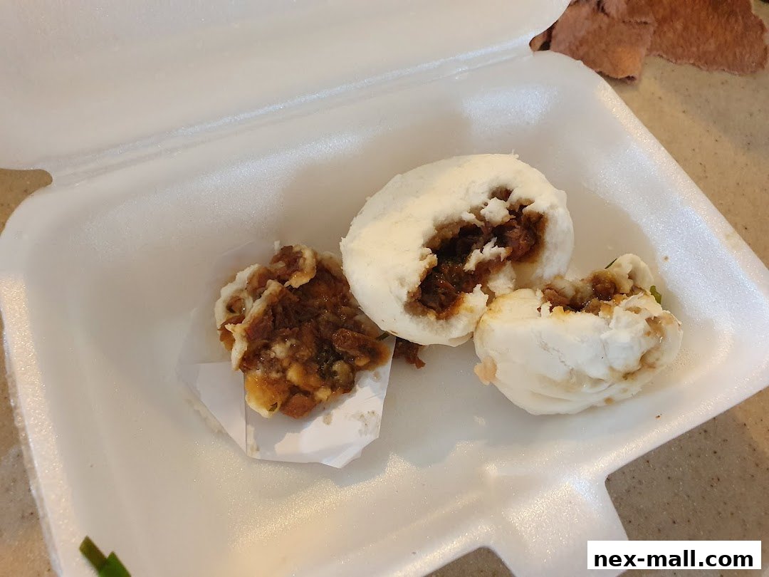 A white styrofoam container holds two steamed buns filled with savory meat.