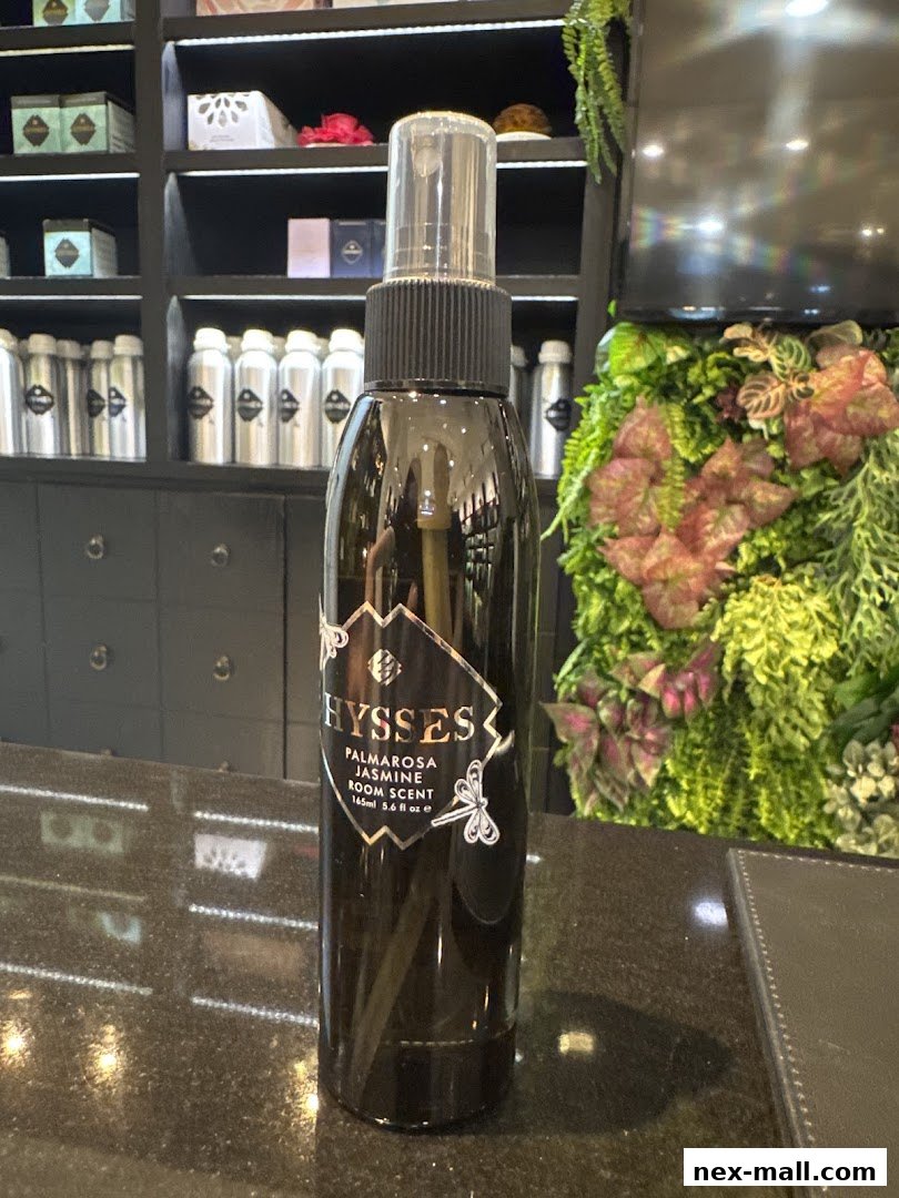 A bottle of HYSSES Palmarosa Jasmine Room Scent sits on a counter with shelves of products behind it.