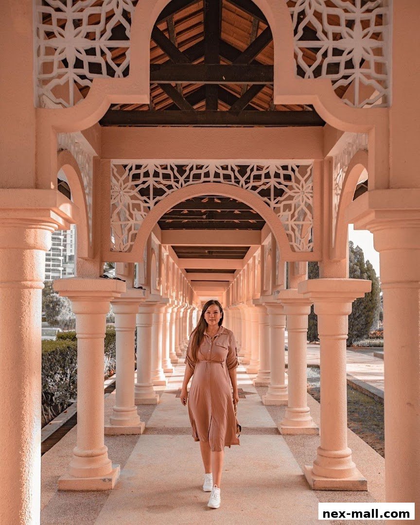 A woman walks down a sunlit, ornate corridor with columns and decorative arches.