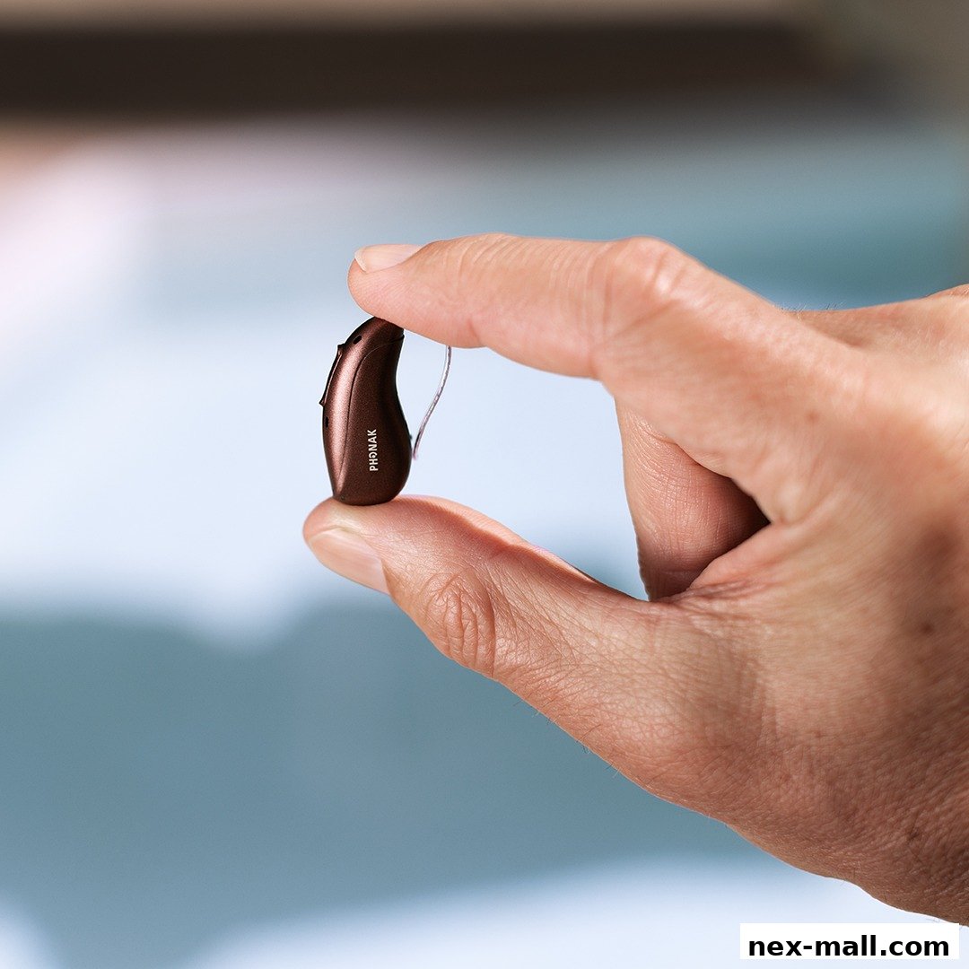 A hand holds a small, brown Phonak hearing aid.