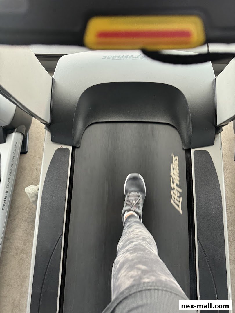 A person's legs and feet walking on a treadmill at Anytime Fitness.