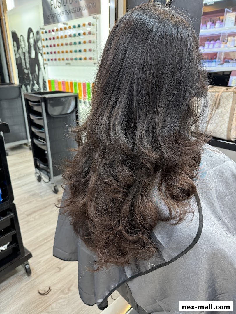 A person's dark, wavy hair is styled in a salon, with hair products visible in the background.