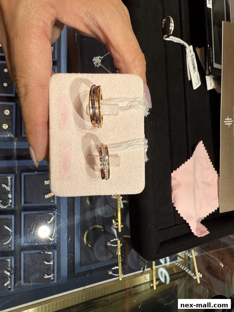 A hand holds two elegant rings, one gold and one diamond-studded, in a jewelry store.