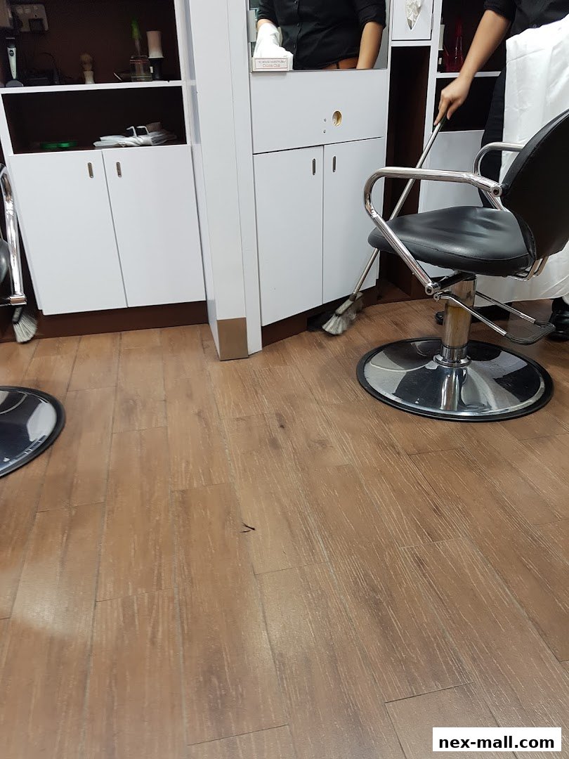 A person is sweeping the floor in a salon with styling chairs and cabinets.