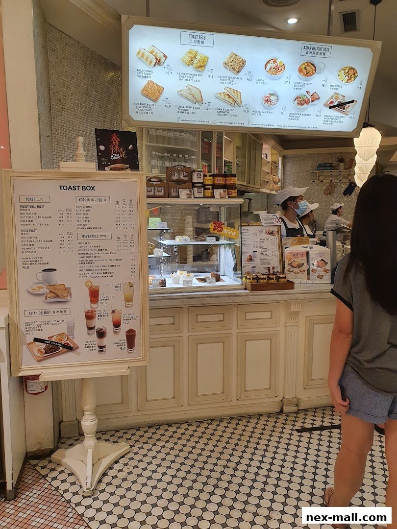 A menu board and display counter at Toast Box NEX, showcasing various toast sets and Asian delights.